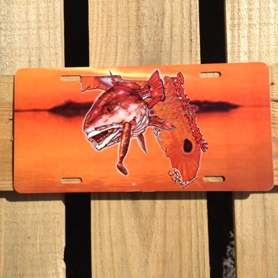 Redfish Republic License Plate: Sunset water/mangroves background with overlaid design of handwritten redfish republic in red, redfish with DOA lure in mouth, and florida state shape filled with redfish scales and spot.